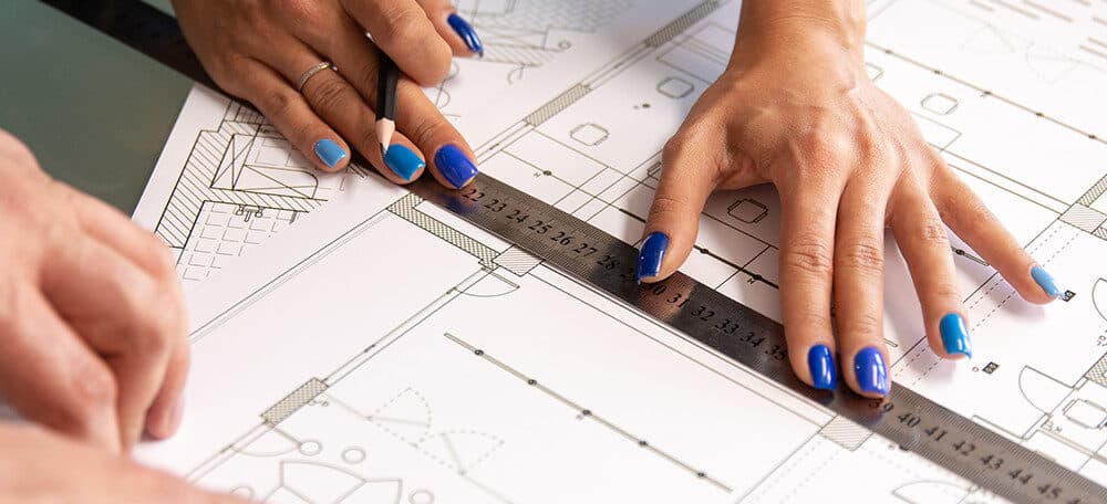 Close-up of architects' hands using a ruler and pencil to analyse a CAD-generated house plan.
