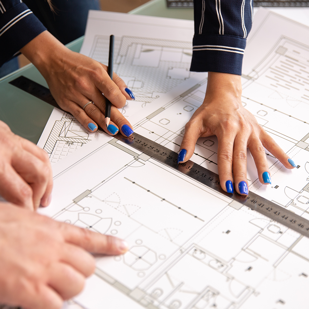Close-up of architects' hands using a ruler and pencil to analyze a CAD-generated house plan.